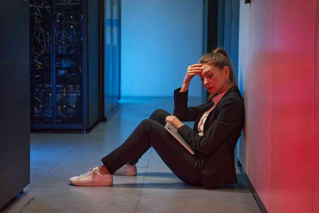 Frustrated female IT manager worry and feel failure while sitting in hallway of datacenter