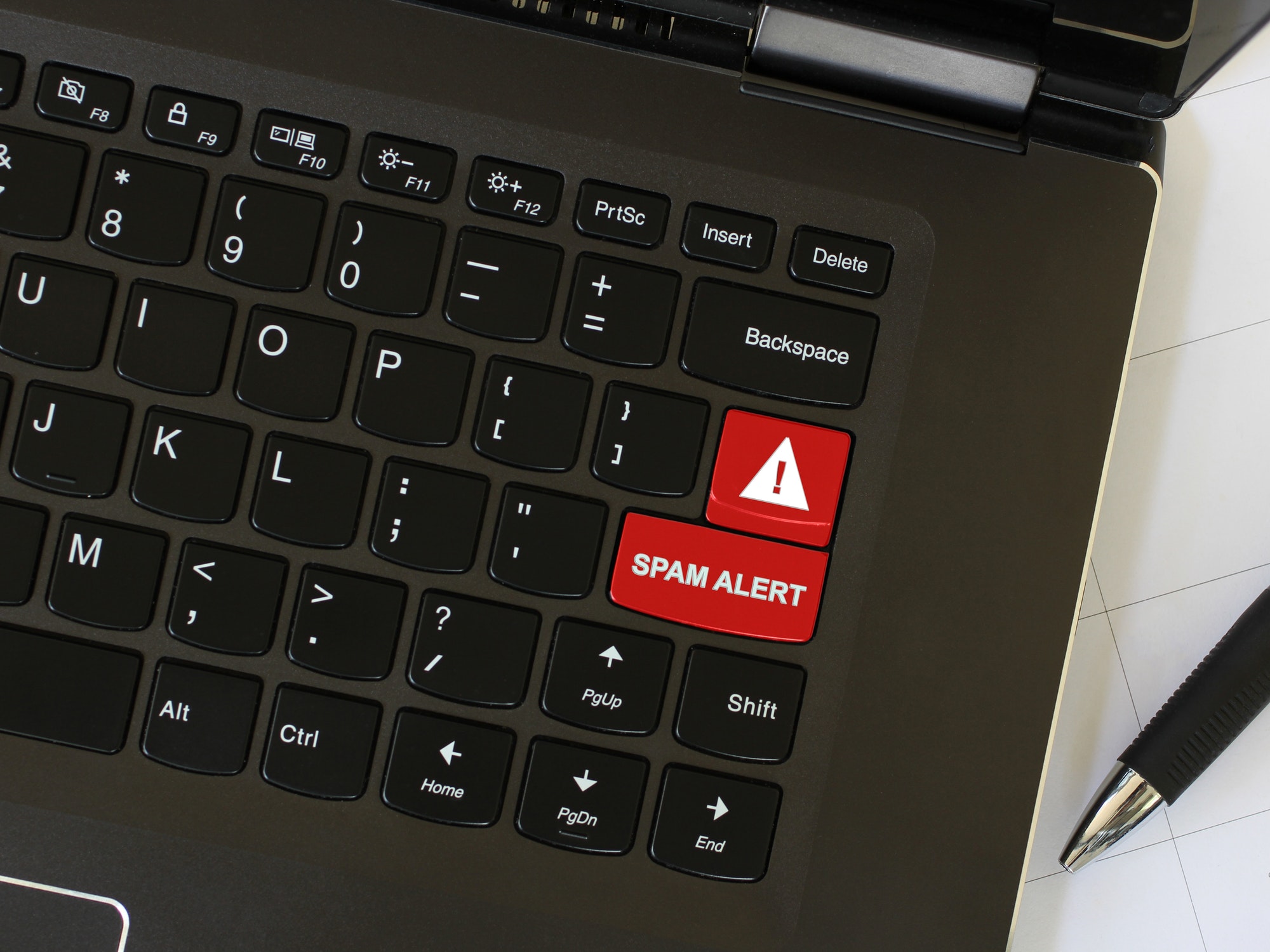 Laptop on workspace area with cyber security red keyboard key with Spam Alert warning written on it